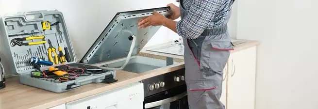 Cooktop repair technician lifting a built-in stovetop for service in Salt Lake City, UT