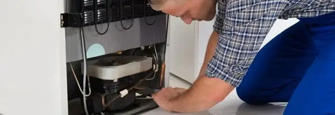Refrigerator repair technician servicing the compressor and condenser area in Salt Lake City, UT