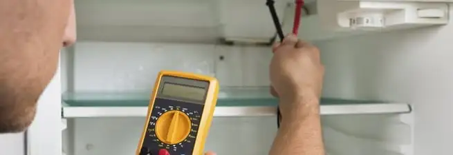 Refrigerator repair technician testing electrical components with a multimeter in Salt Lake City, UT